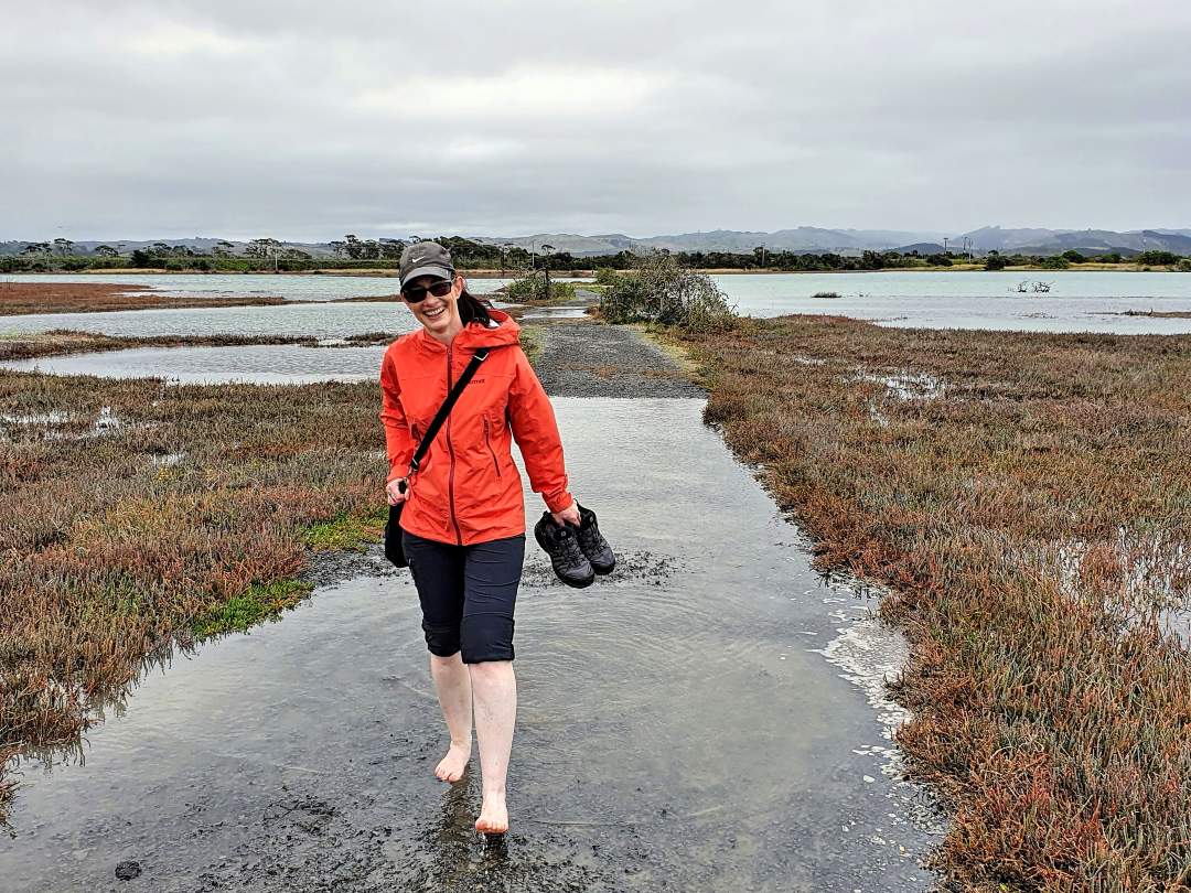 Person walking barefoot through marsh holding shoes