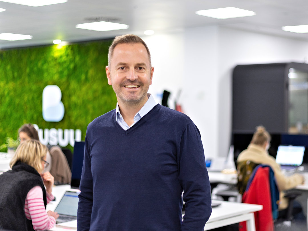 bernhard niesner busuu co founder Bernhard Niesner standing in a modern office space with the Busuu logo visible in the background and people working at desks