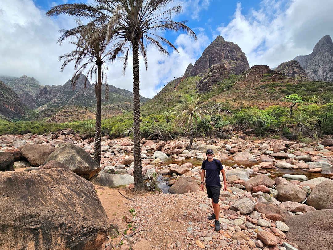 crossing a wadi in the hajhir mountains Hiker in rocky desert landscape with palm trees.