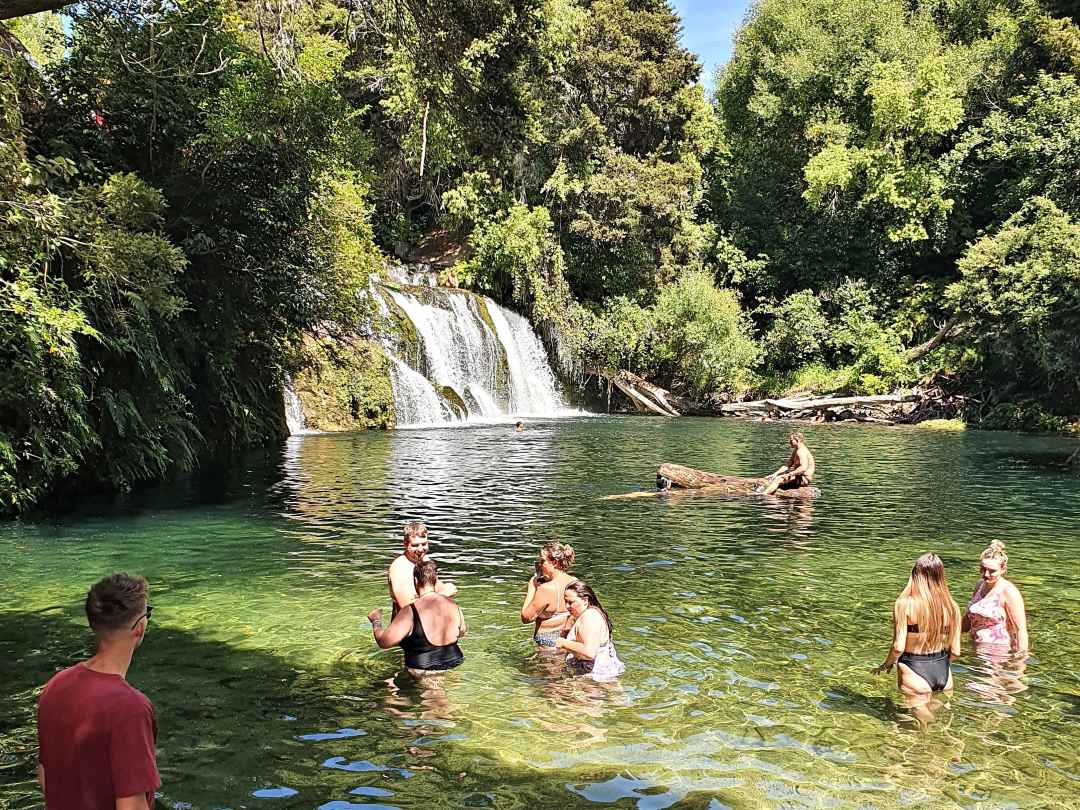 People swimming in clear pool beneath waterfall