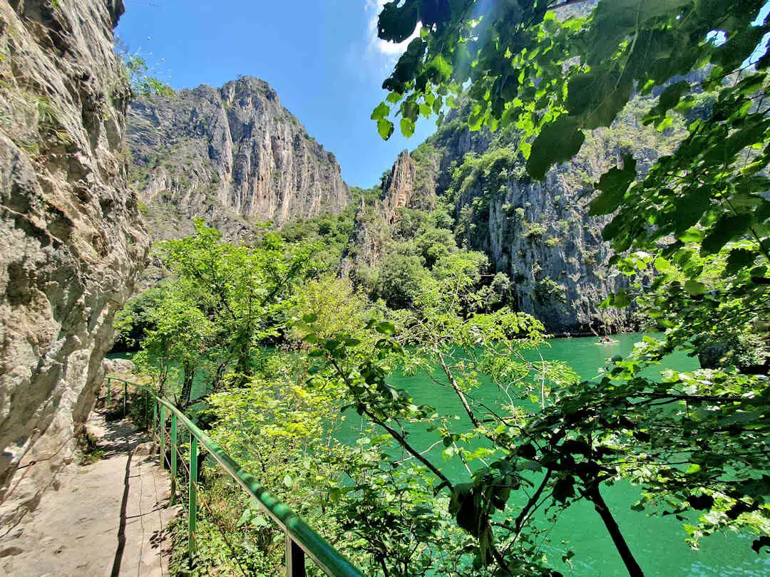 Scenic Cliffside Walk Along the River in Matka Canyon Cliffside walking path above emerald green water in Matka Canyon, surrounded by steep rock faces and lush forest