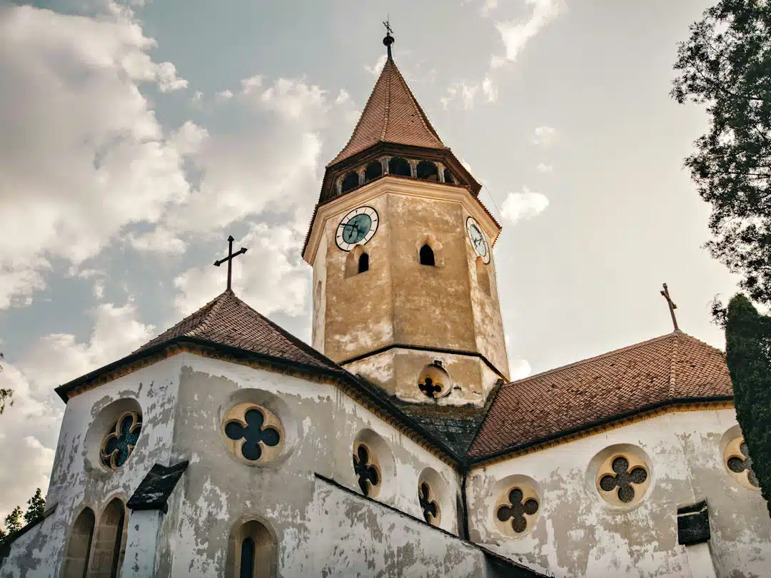 prejmer fortified church by anton darius on unsplash Exterior of Prejmer Fortified Church with Clock Tower and Crosses under a Cloudy Sky
