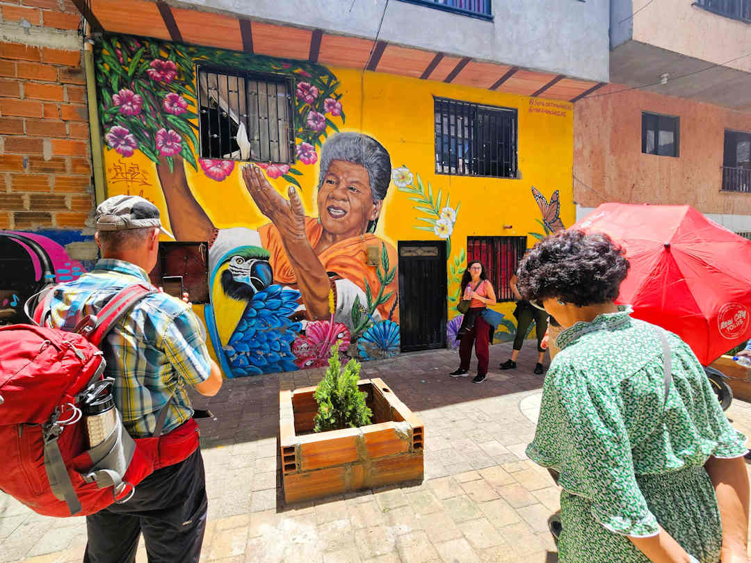 Mural celebrating community resilience in Moravia, Medellín Visitors viewing a colourful mural of a woman with flowers in Moravia during the Comuna 4 walking tour