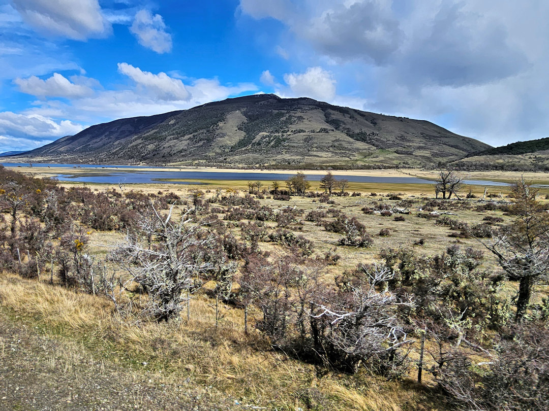 Shrubland, a lake, and a low mountain under changing skies in southern Patagonia.