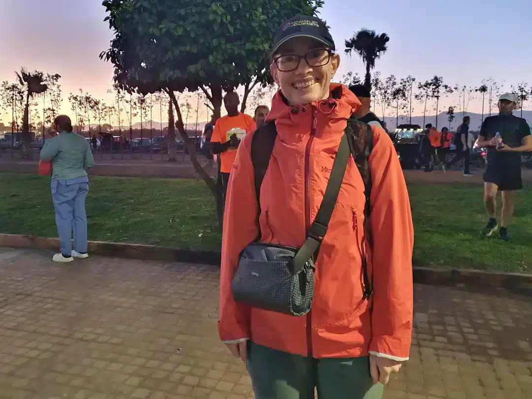 Woman in red jacket smiling at park during sunset.