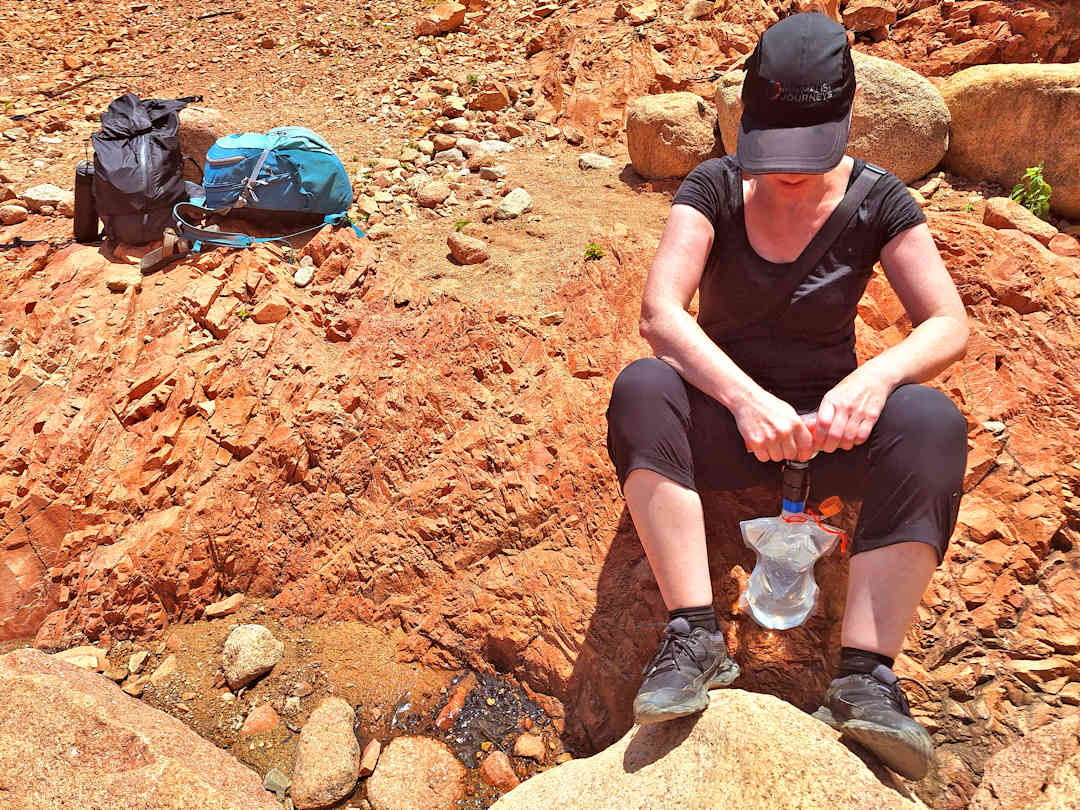 Woman Filtering Spring Water with a Squeeze Filter Kit While Hiking in Socotra