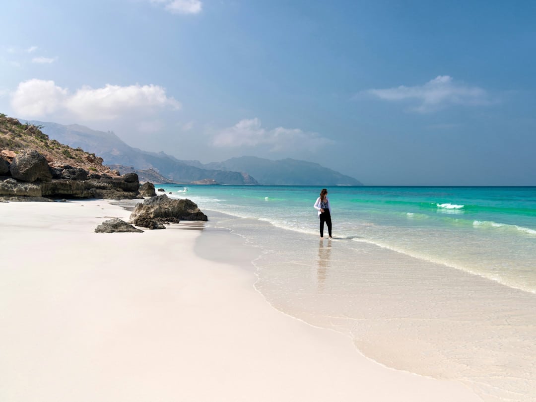 shoab beach by andrew svk on unsplash Woman walking on scenic beach with turquoise water.