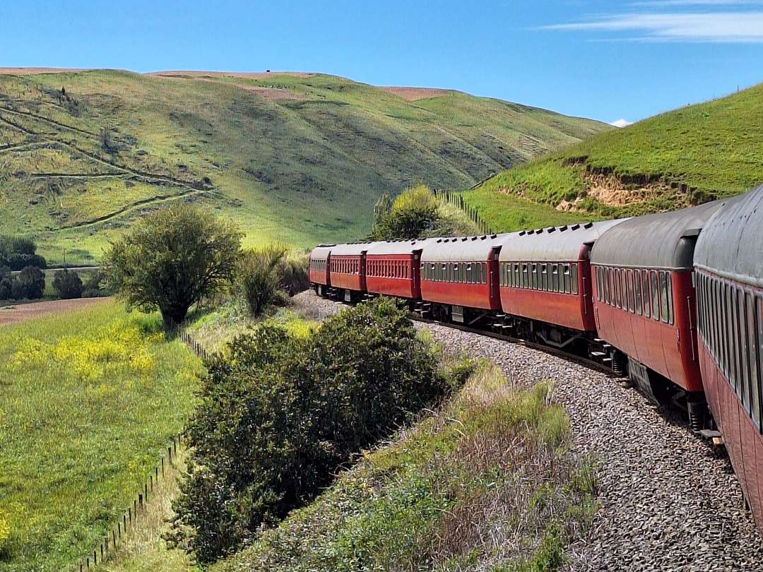 Red passenger train winding through green hills