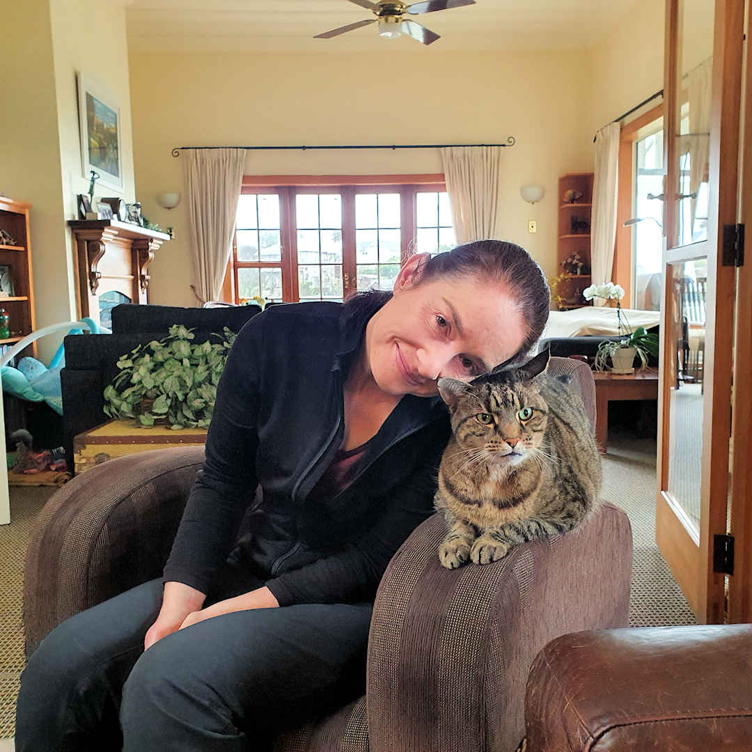 Sandra sitting beside Tigger, a tabby cat, on an armchair, both looking content and relaxed.