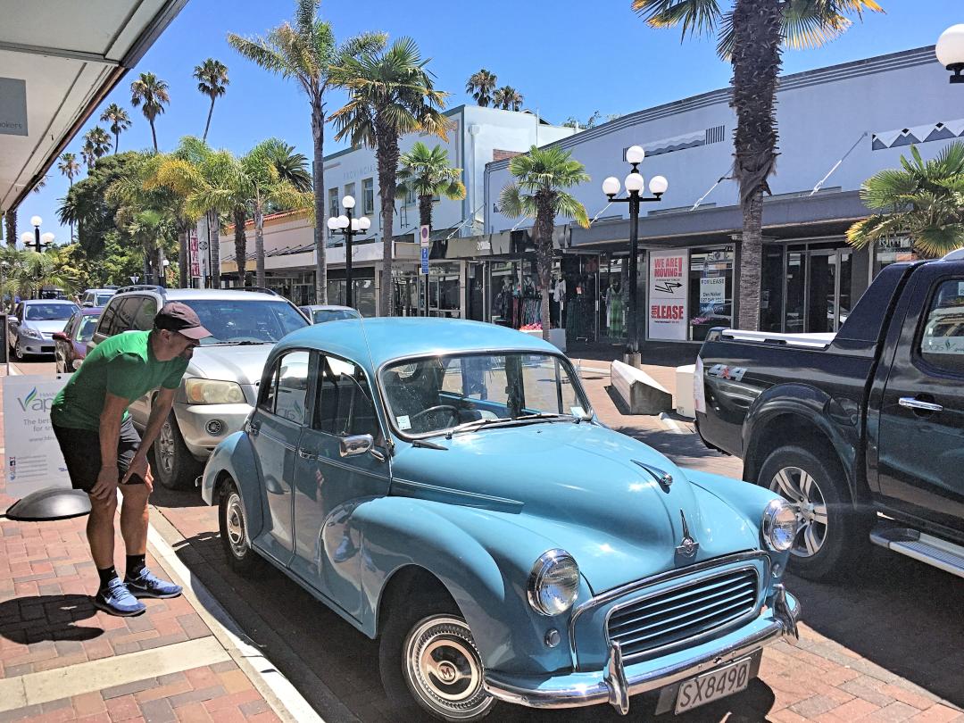 Man admiring vintage blue car on sunny street