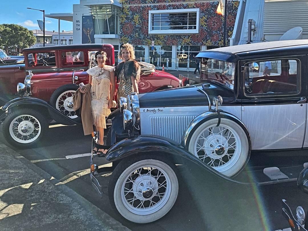 Women in 1920s outfits beside vintage cars