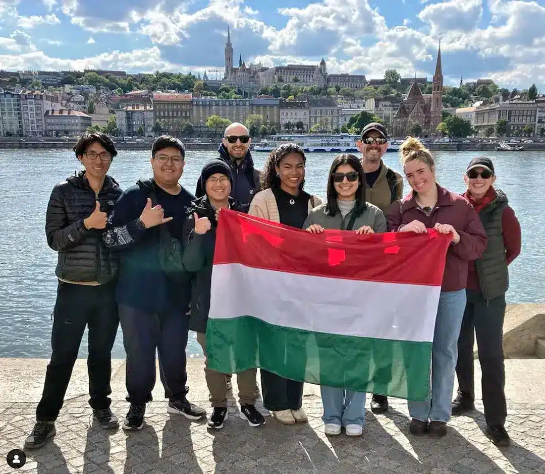 Walking Tour Budapest Group holding a red, white, green flag by river.